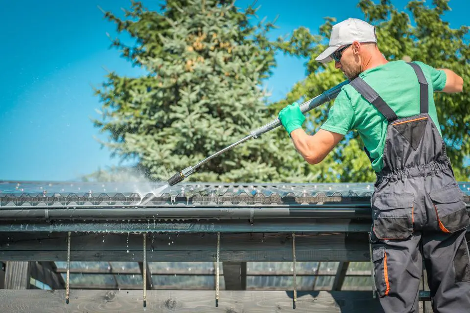 gutter cleaning-man standing on ladder power washing gutter system on house