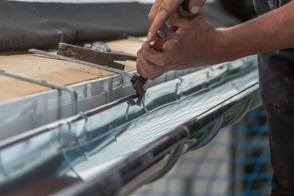 gutter repair-close up of a man using hand tools to repair a section of metal gutters