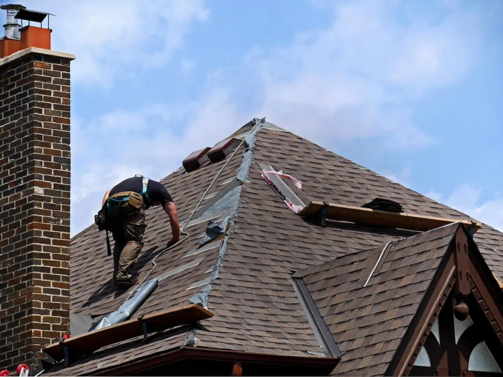 man working on roof repair on a roof in columbus with a brown brick chimney and blue sky in background