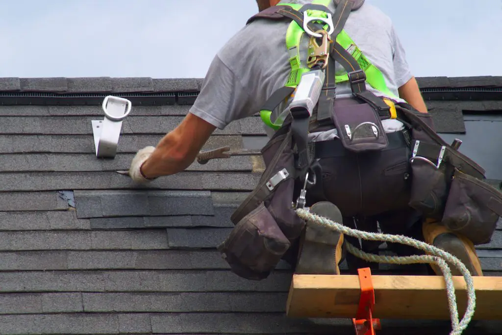 Roofing contractor wearing safety harness and tool belt making asphalt shingle repairs on a residential roof in Upper Arlington, Ohio.