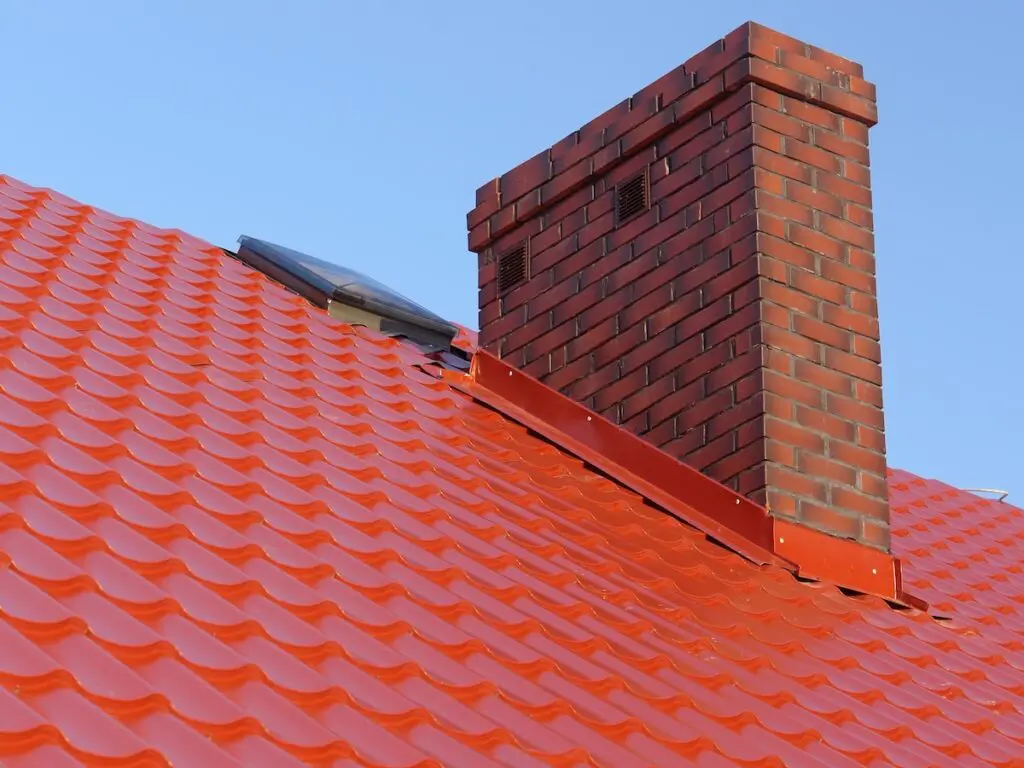Closeup of red roof metal covering with brick-made chimney