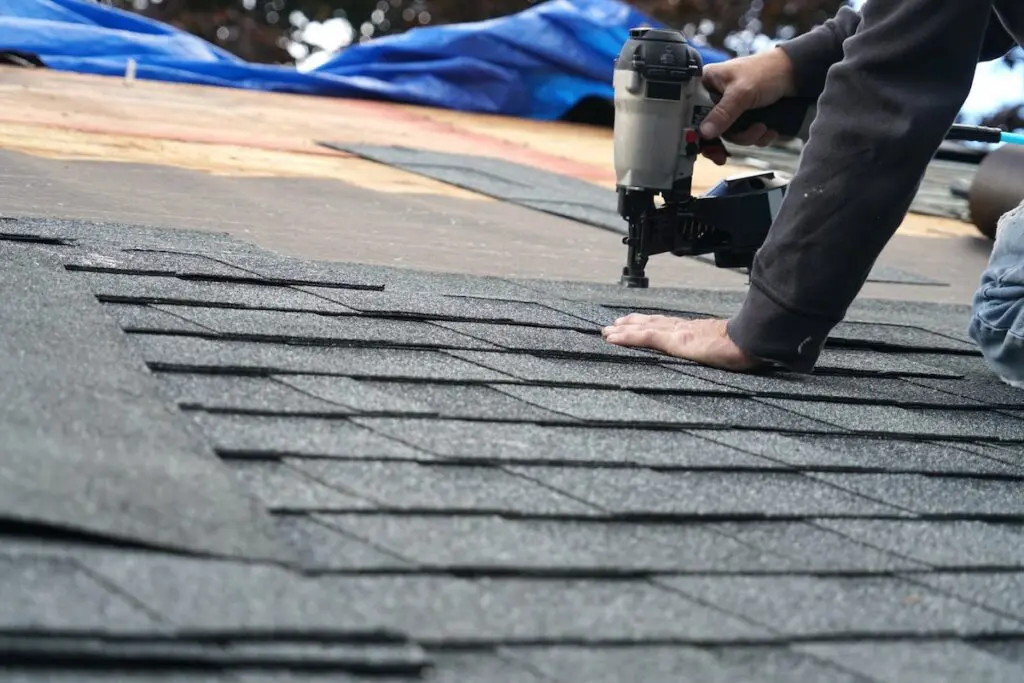handyman using nail gun to install shingle to repair roof