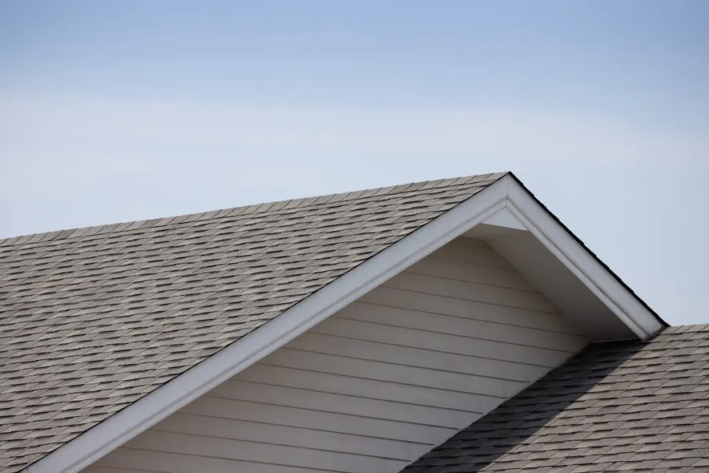 Roof shingles on top of the house against blue sky with cloud, dark asphalt tiles on the roof background