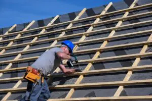 Repair and replacement of the old roof with a new one. Construction worker in protective clothing standing on roof with tools.