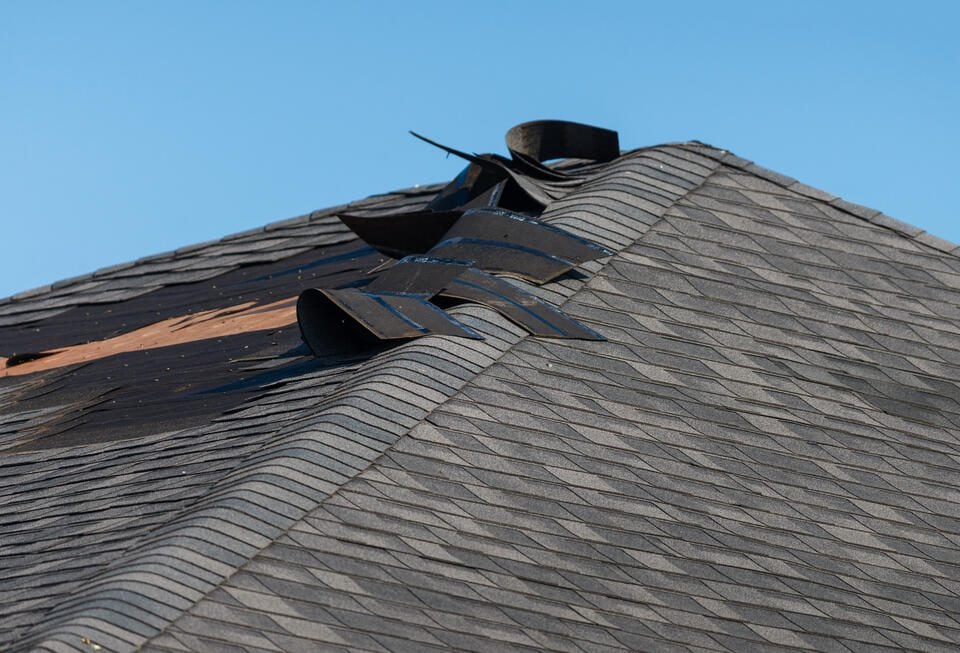 wind damage to roof-close up of lifted shingles on a gray roof