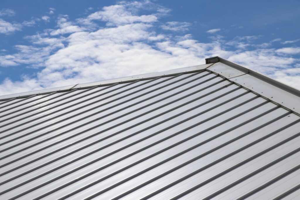 What Is A Standing Seam Metal Roof? & Key Benefits - All Phase Roofing & Restoration Metal sheet roof and slope with clouds and blue sky background.