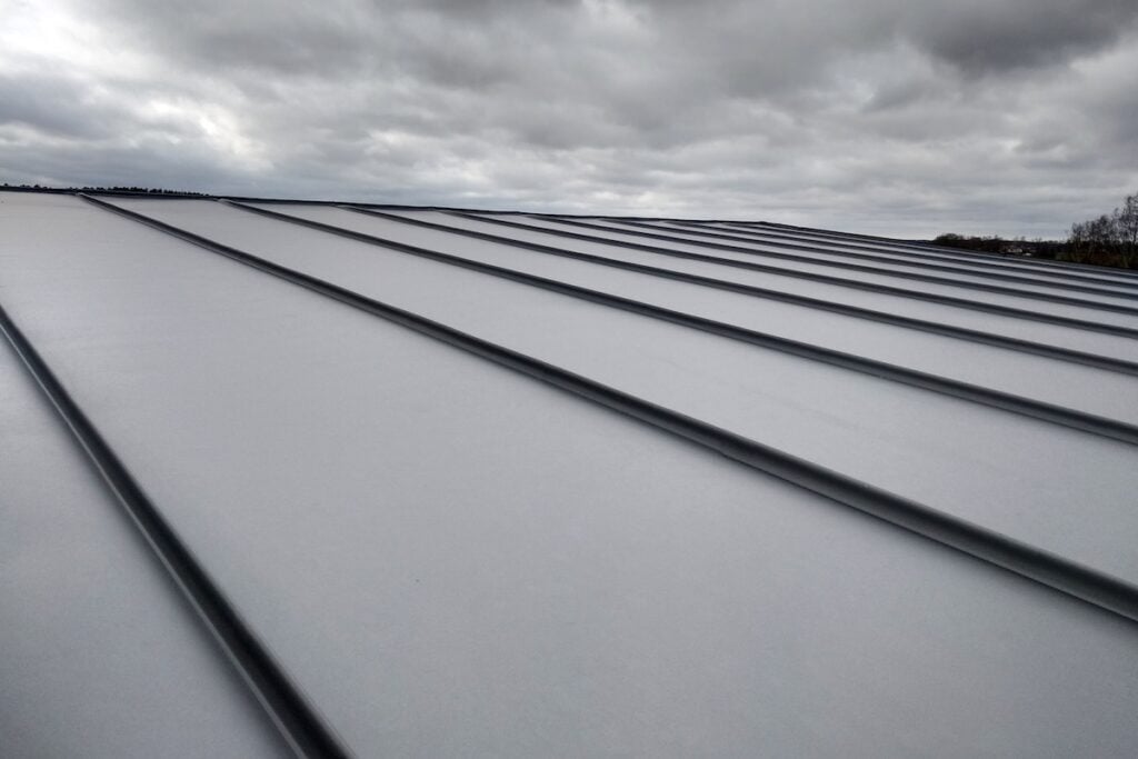 What Is A Standing Seam Metal Roof? & Key Benefits - All Phase Roofing & Restoration Close-up detail of house roof made from gray metal sheets.