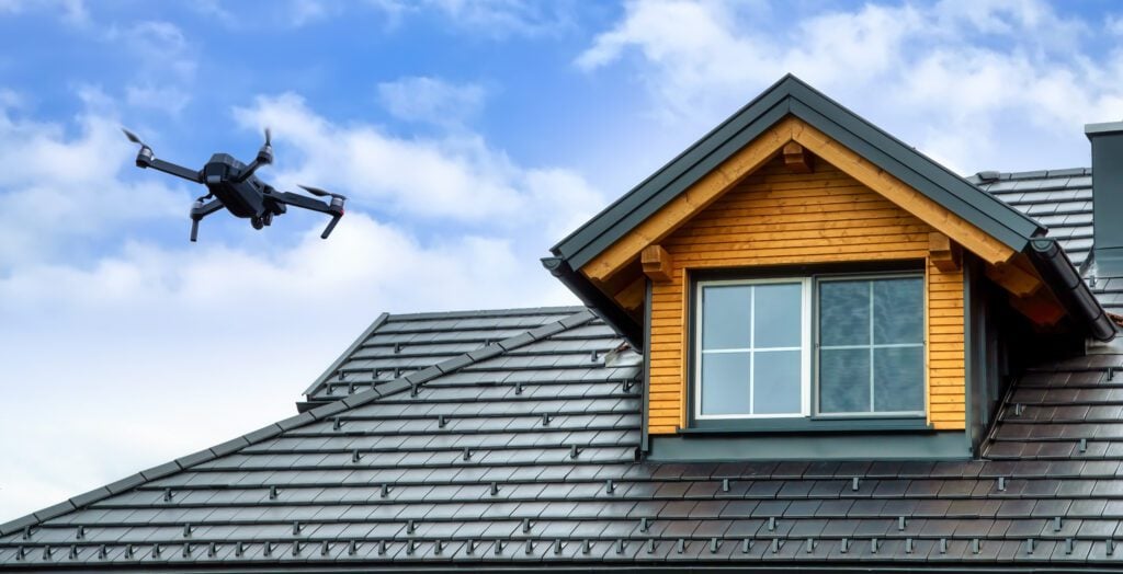 Drone Roof Inspection: What Are The Top 4 Benefits? - All Phase Roofing & Restoration Drone in the air inspecting the roof over the house. Close-up of drone and roof. drone roof inpsection