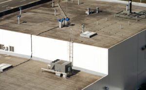 Our Service Areas - All Phase Roofing & Restoration Fragment of the roof of a commercial building with a external units of the commercial air conditioning and ventilation systems.