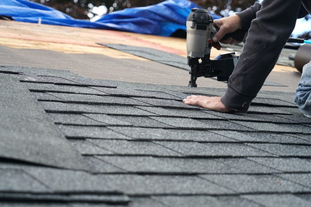 Roof Restoration vs Replacement (5 Key Differences) - All Phase Roofing & Restoration handyman using nail gun to install shingle to repair roof